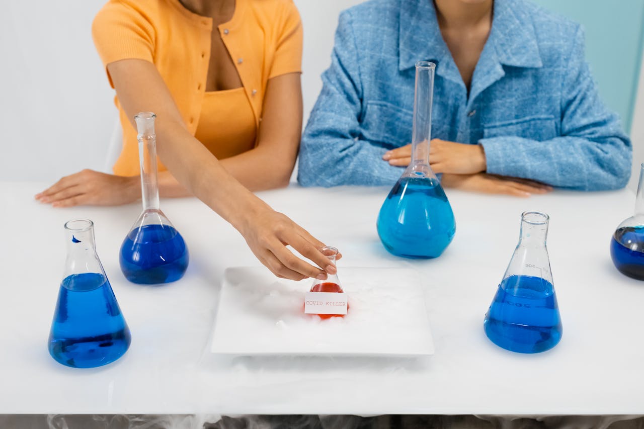 Two women in a laboratory setting conducting an experiment, using Erlenmeyer flasks containing blue liquid.